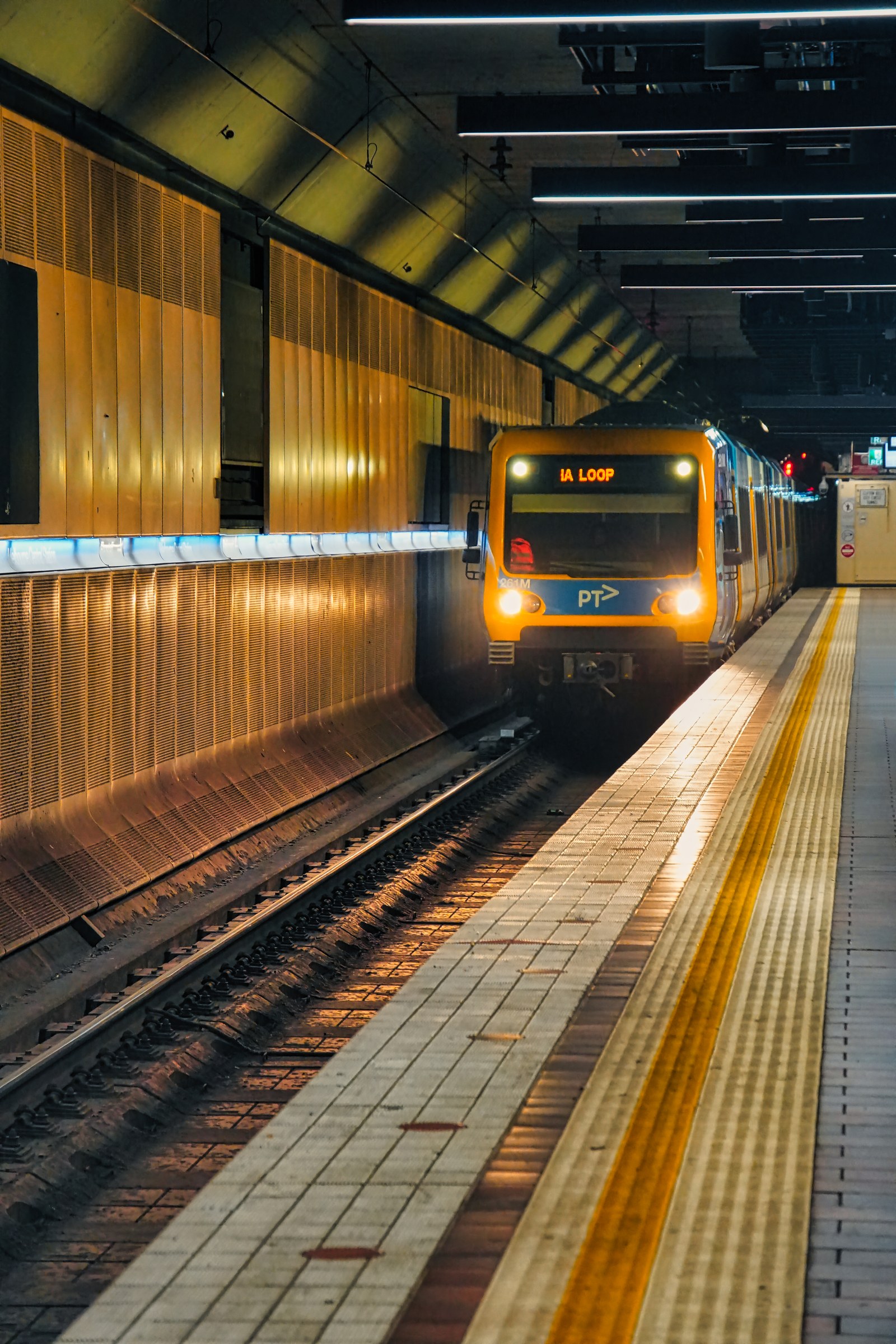 A yellow-fronted train approaches a platform in a warmly lit underground station.