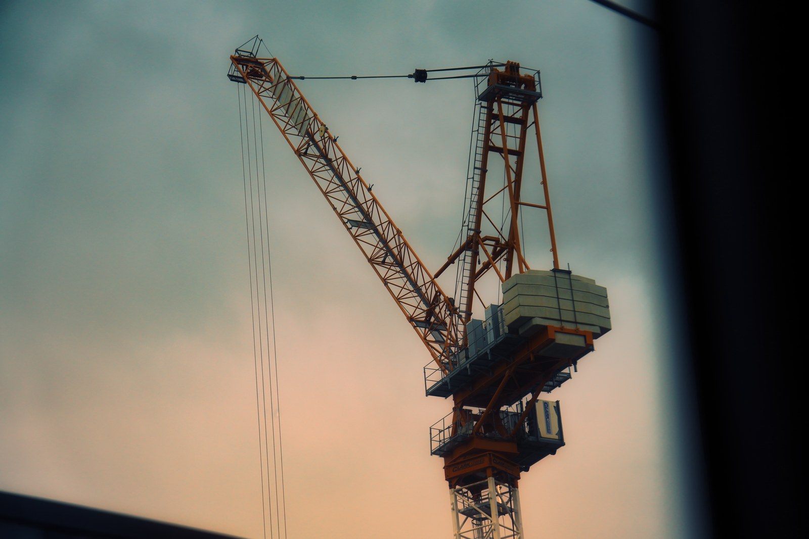 A construction crane is framed by dark edges against a softly coloured sky.