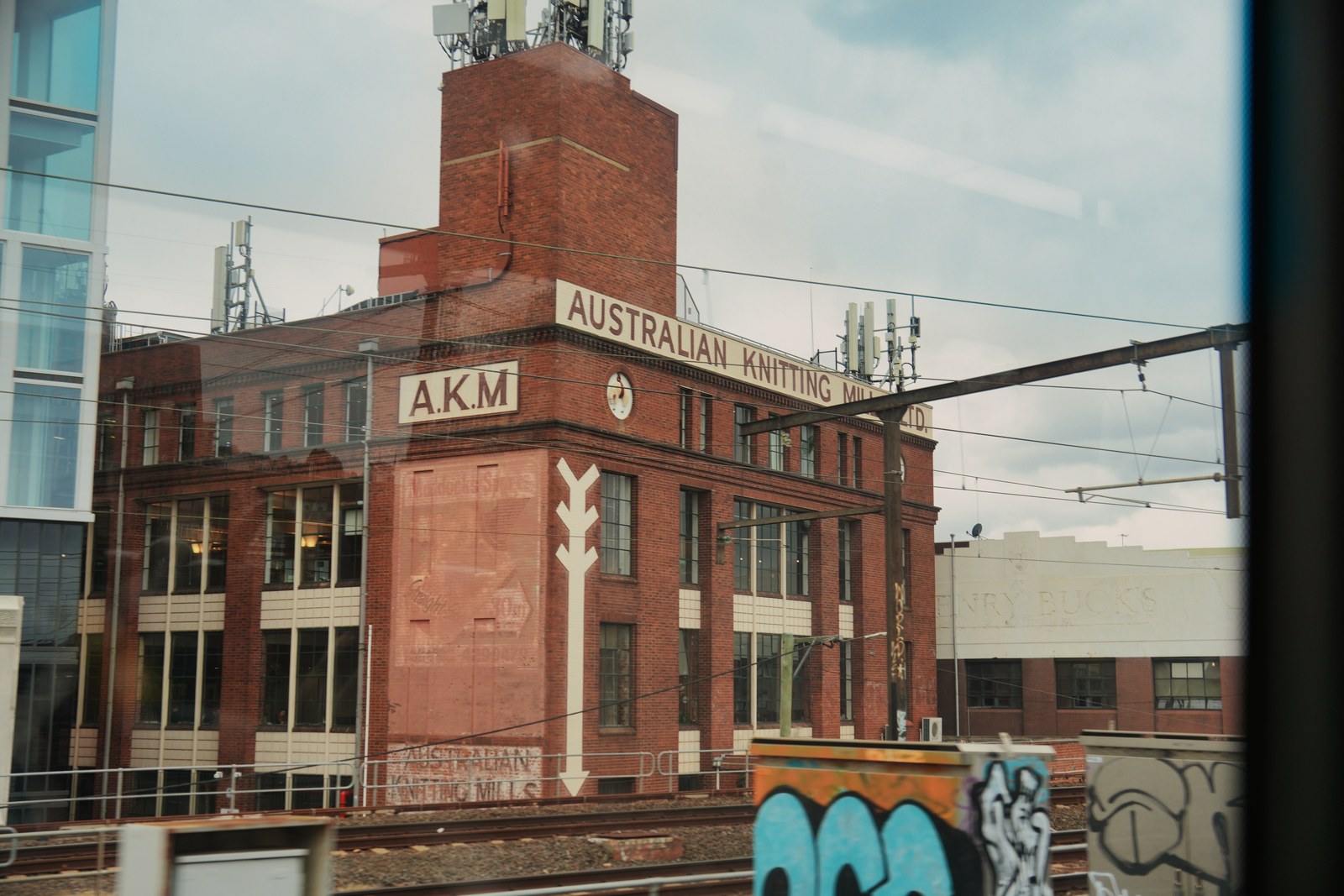A red brick building marked Australian Knitting is crossed by overhead wires, with graffiti below.