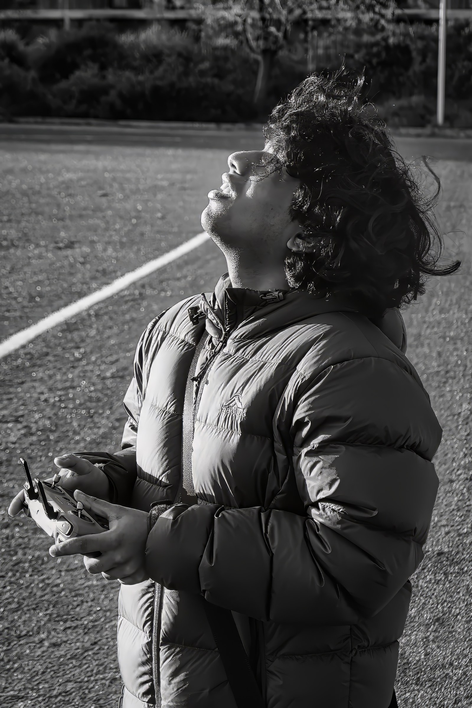A monochrome portrait of a curly-haired person looking upward while holding a controller.