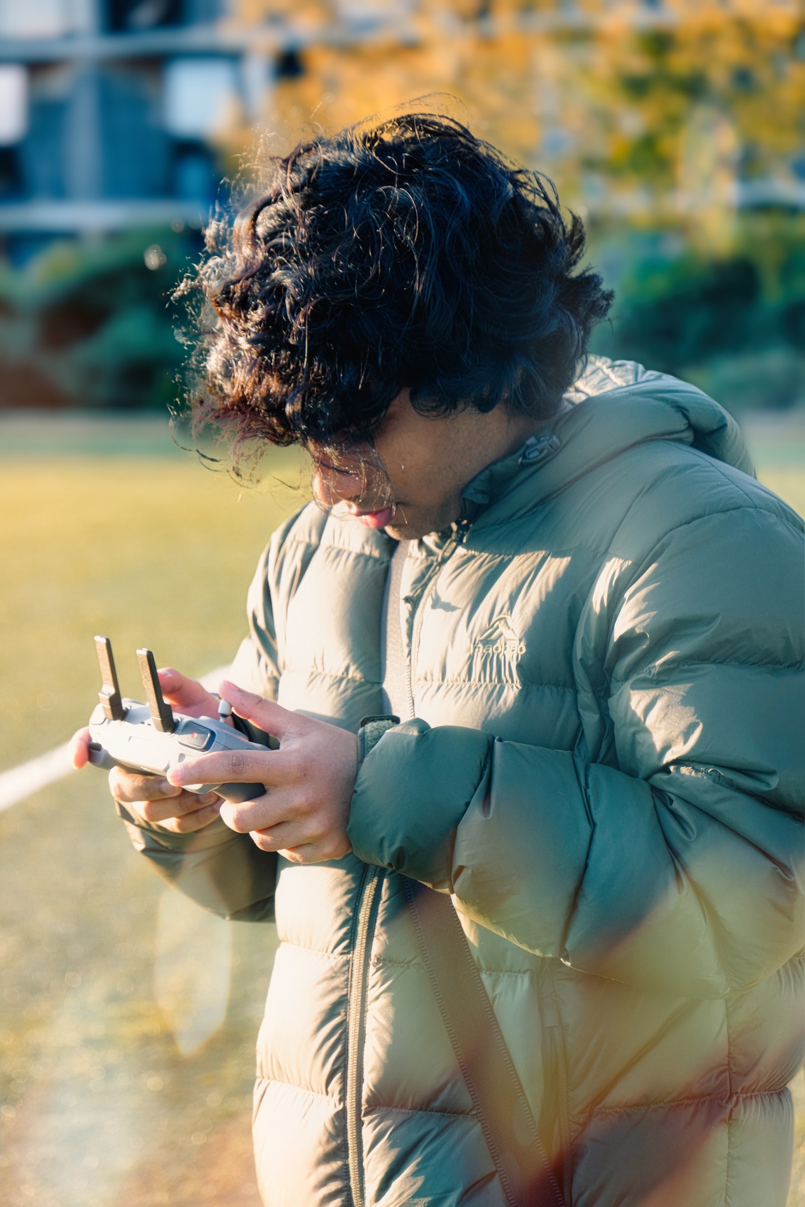 A curly-haired person in a pale padded jacket looks down at a handheld controller.