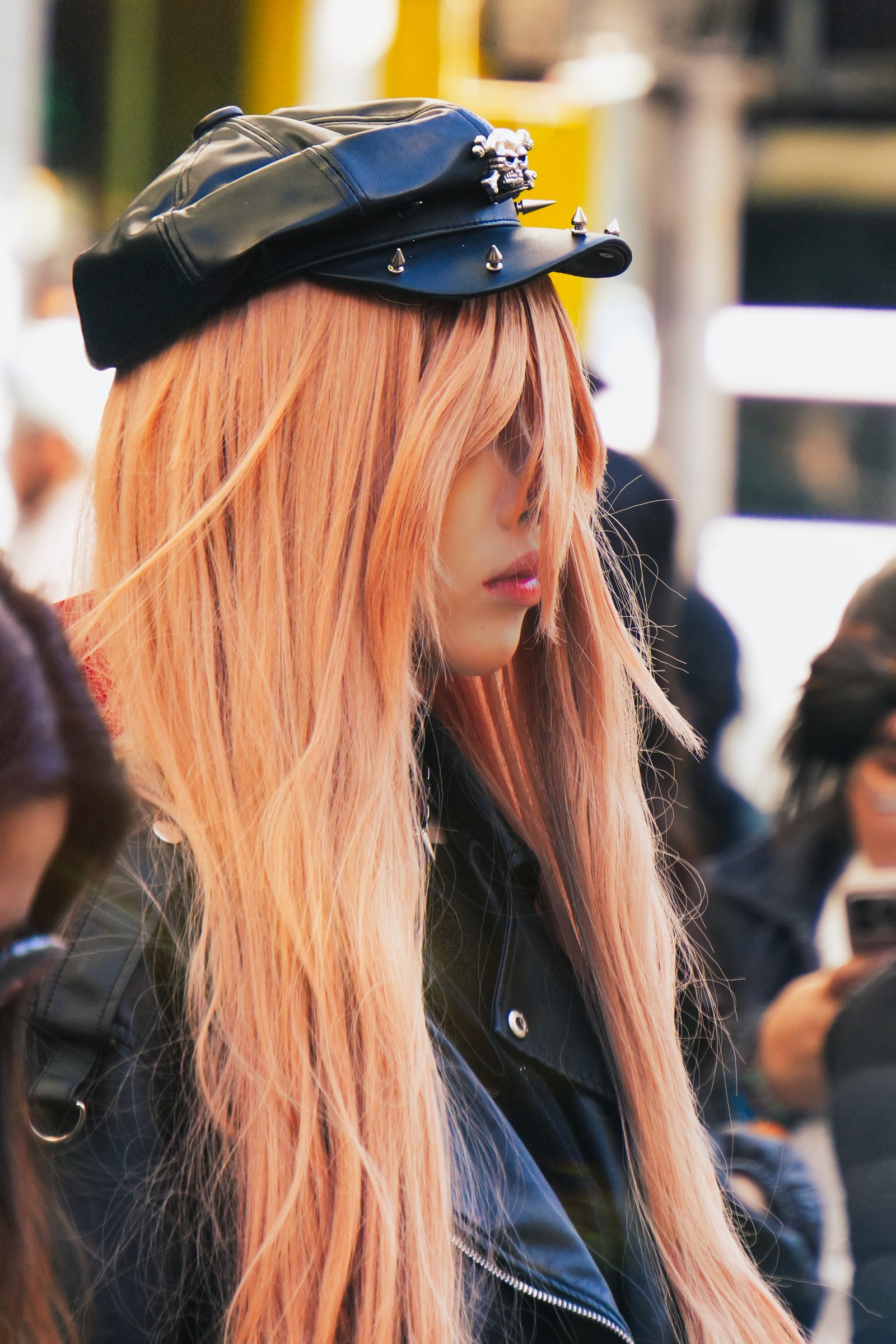 A person with long orange hair and a decorated black cap is shown in profile.